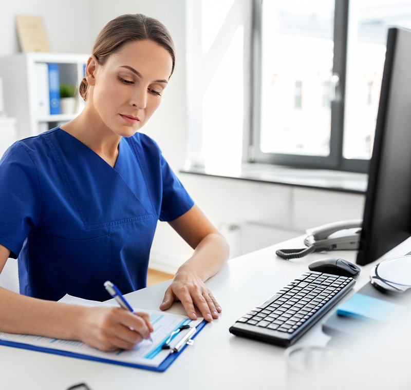 An electronic health records specialist works at a computer in a medical office, updating and managing patient records within a secure digital system.