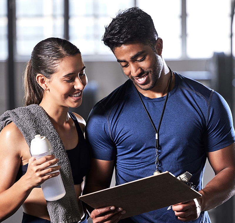 A physical trainer assists a client with strength exercises in a well-equipped gym, providing guidance on proper form and technique to support fitness goals.